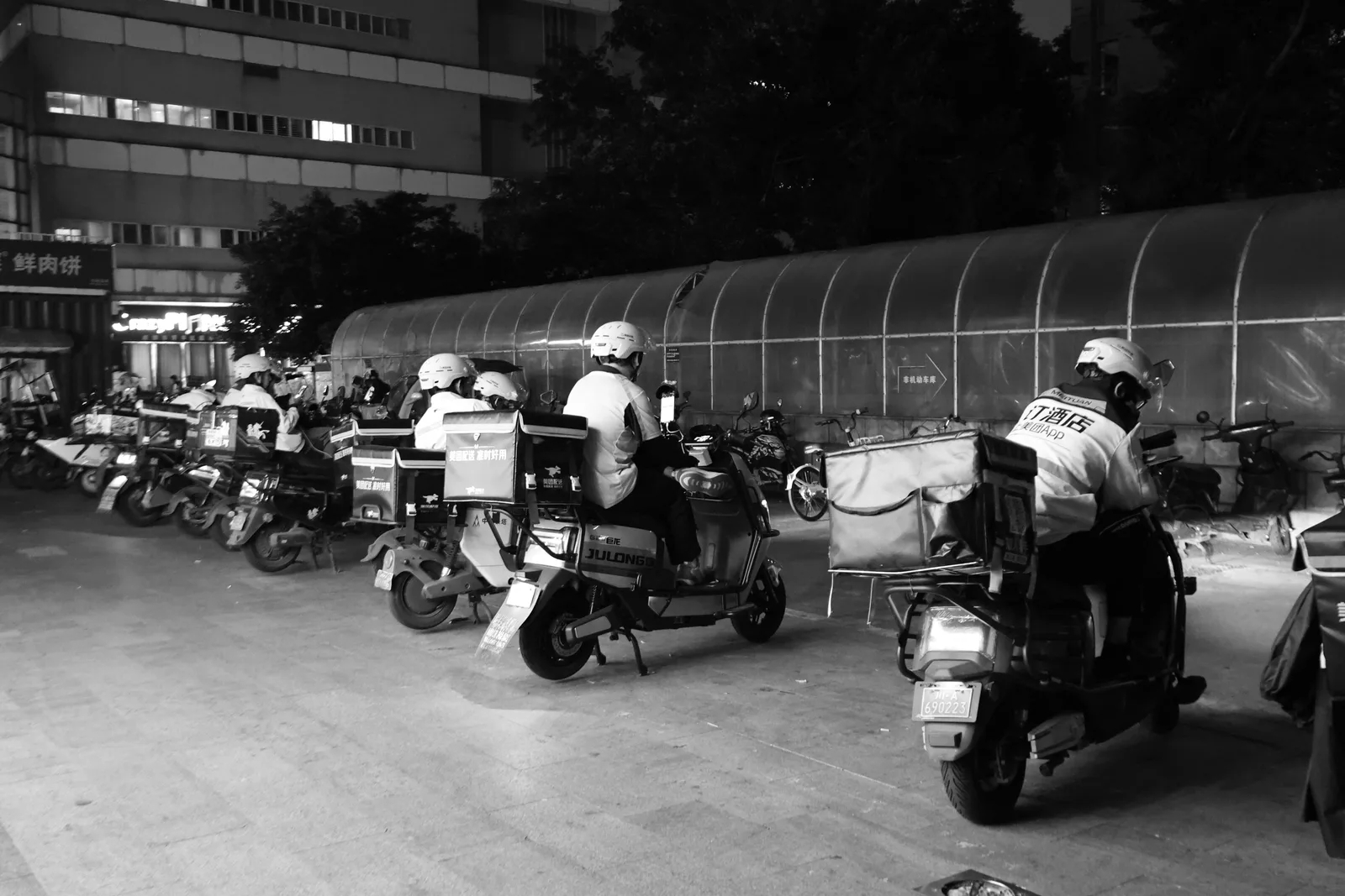 Food delivery drivers on scooters gather at night for dispatch in an urban setting. Which US States Ban Tip Credits for Ghost Kitchen Operations?