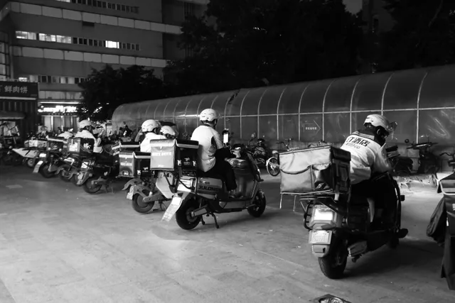 Food delivery drivers on scooters gather at night for dispatch in an urban setting. Which US States Ban Tip Credits for Ghost Kitchen Operations?